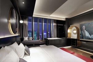 Una habitación de hotel moderna con una cama grande, zona de estar, bañera y una televisión de gran tamaño.