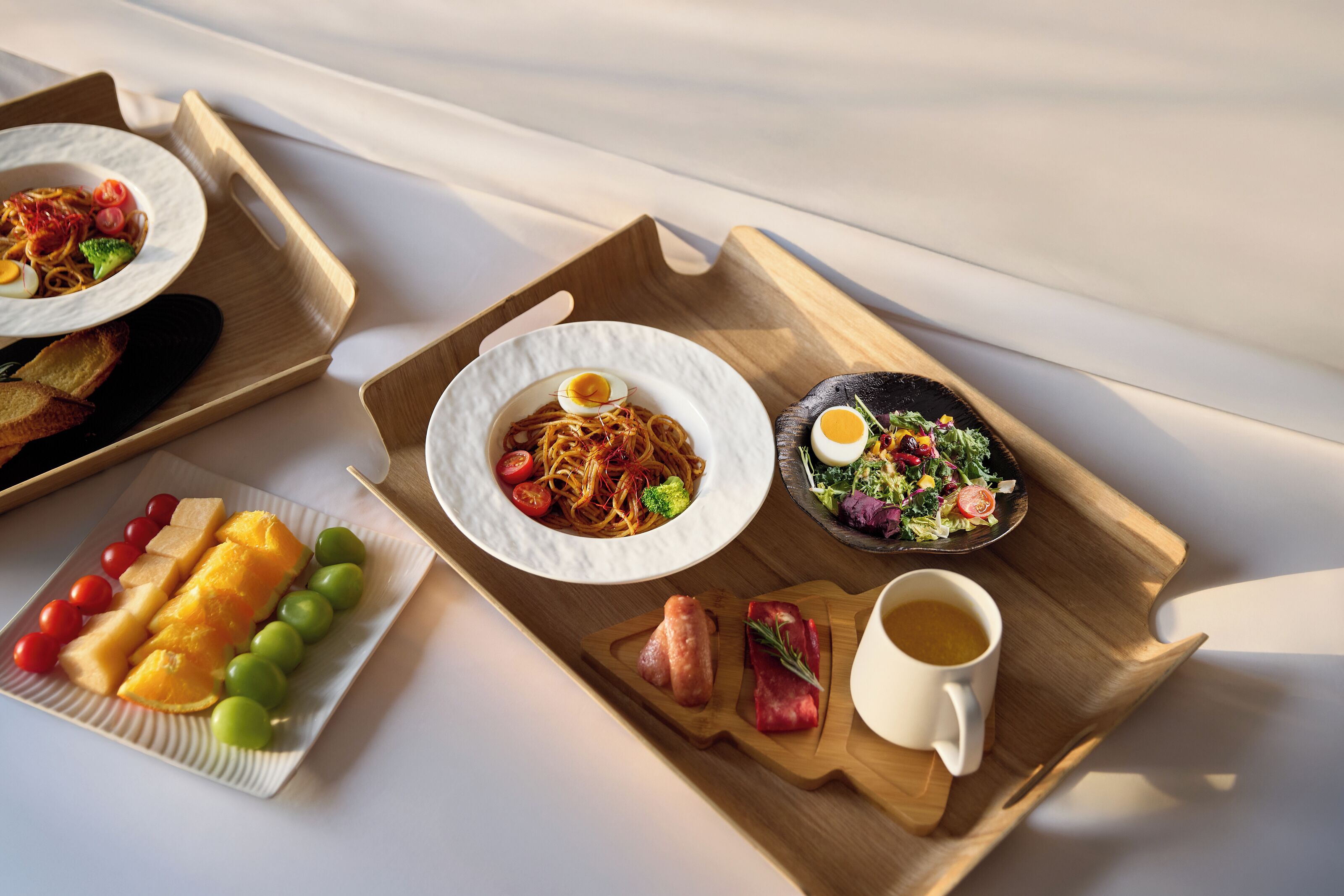 A breakfast tray with various dishes including noodles, eggs, a salad, and fruits.