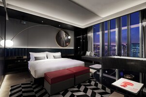 A modern hotel room with a large bed, a desk, and a view of the cityscape.