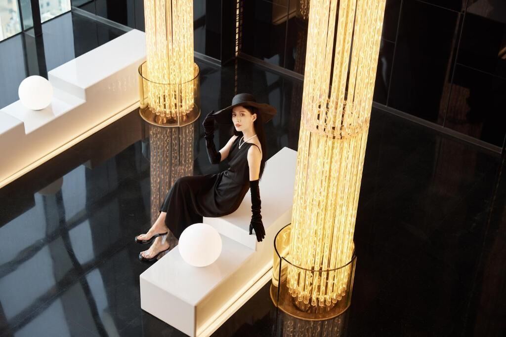Una persona asseguda en un banc blanc en un vestíbul modern amb altes columnes il·luminades i un sòl reflectant.