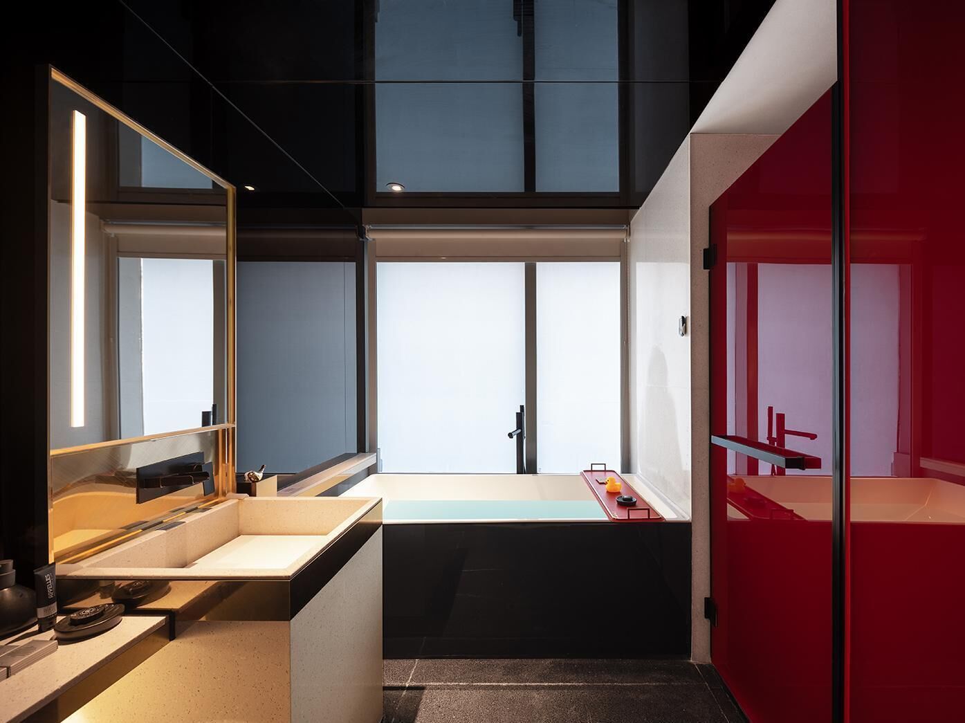 Een moderne badkamer met een grote spiegel, een badkuip en een rode accentmuur.