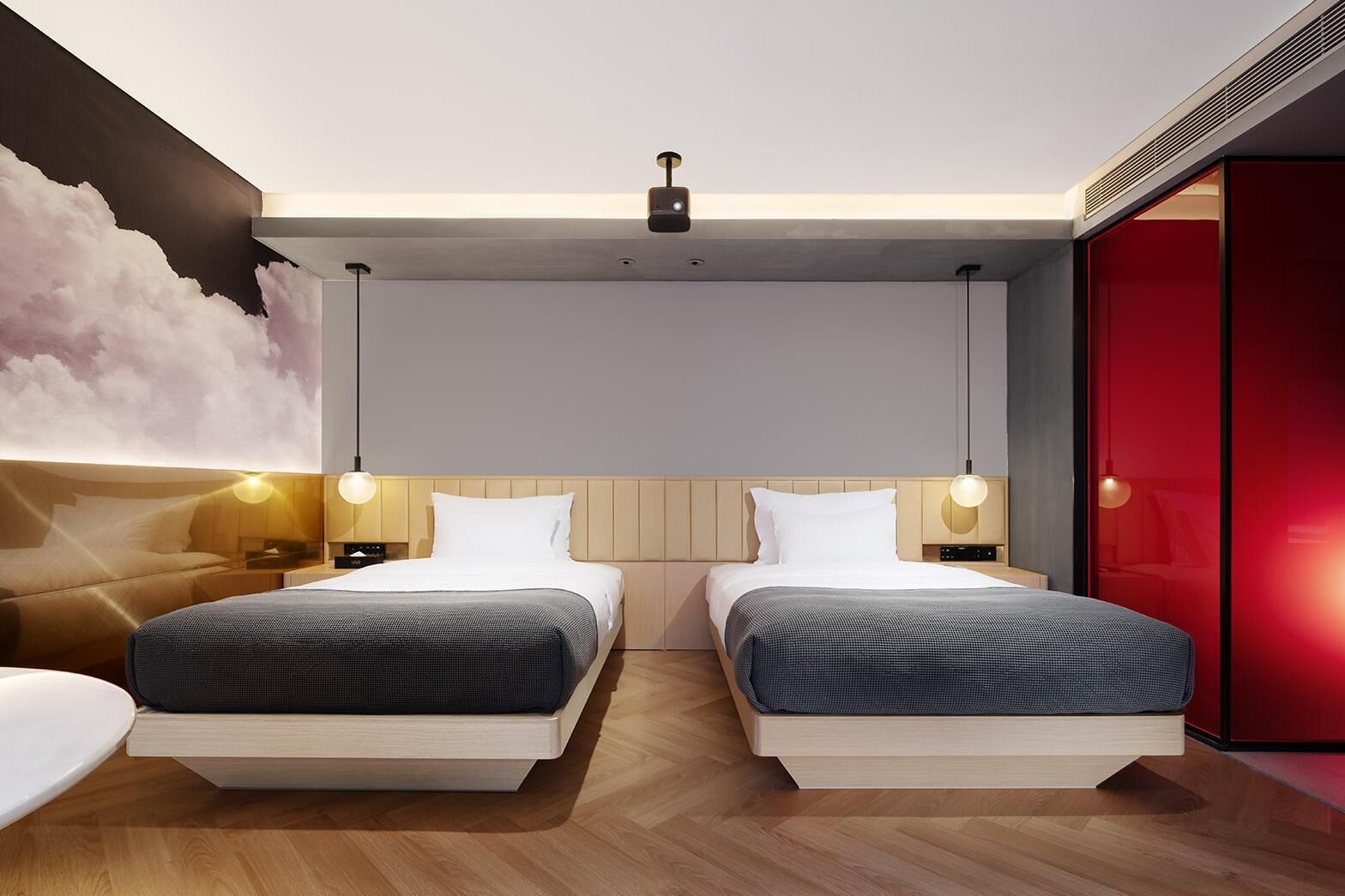 A modern hotel room with two beds, a large wall mural, and a red accent wall.