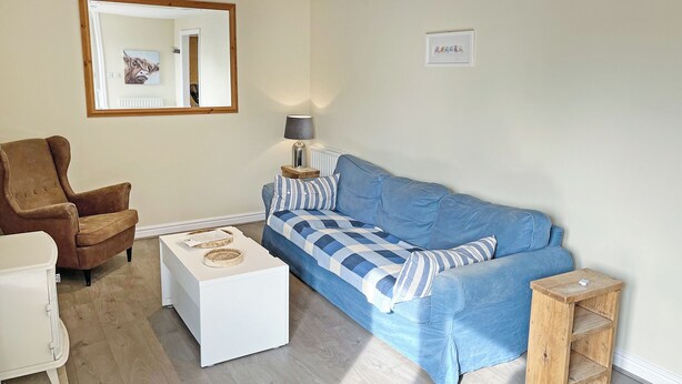 A living room with a blue sofa, a brown armchair, a white coffee table, a wooden side table, and a mirror on the wall. - Elder Cottage - UK51371 (Caldwell, Richmond)