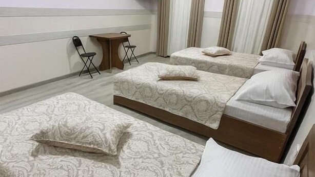 Habitación de hotel con tres camas, un escritorio, una silla y un equipo de aire acondicionado.
