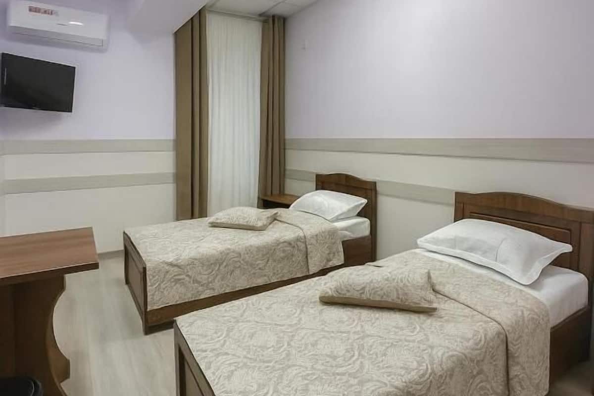 A hotel room with two beds, a desk, a chair, a TV, and a window with curtains.