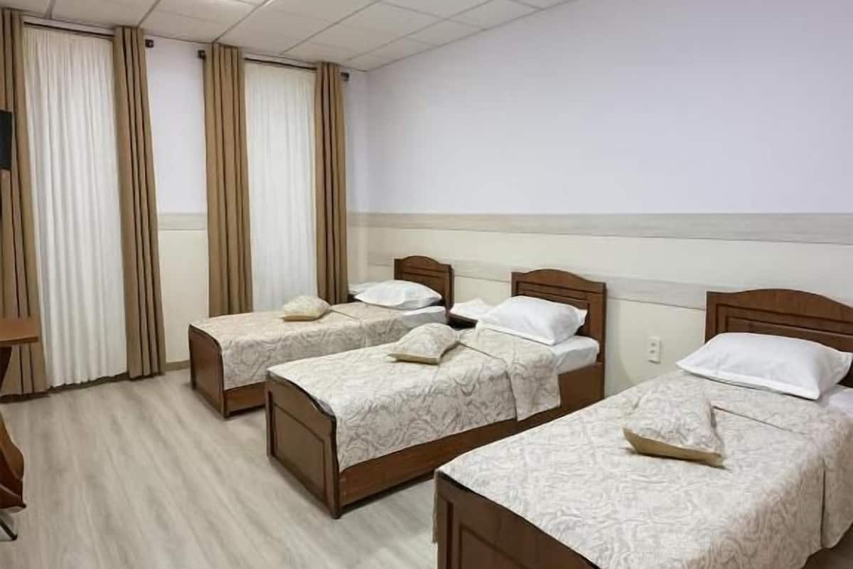 A hotel room with three wooden beds, a wooden desk, and a large window with curtains.