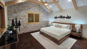 Ein Schlafzimmer mit Steinwand, Holzbalken, einem Bett, Nachttischen und einem Deckenventilator.