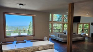Eine moderne Küche mit einem großen Fenster, einem Essbereich und einem Wohnzimmer mit einer Couch und einem Fernseher.