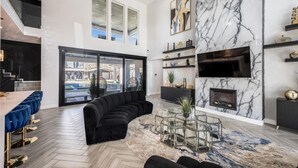 A modern living room with a curved black sofa, a glass coffee table, a fireplace, and a large window overlooking a cityscape.
