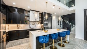 A modern kitchen with dark cabinetry, a marble island, and blue bar stools.