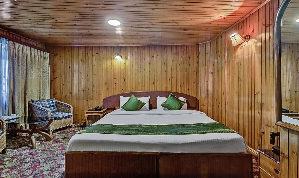 Quarto com painéis de madeira, uma cama, duas cadeiras, uma mesinha de cabeceira e um espelho.