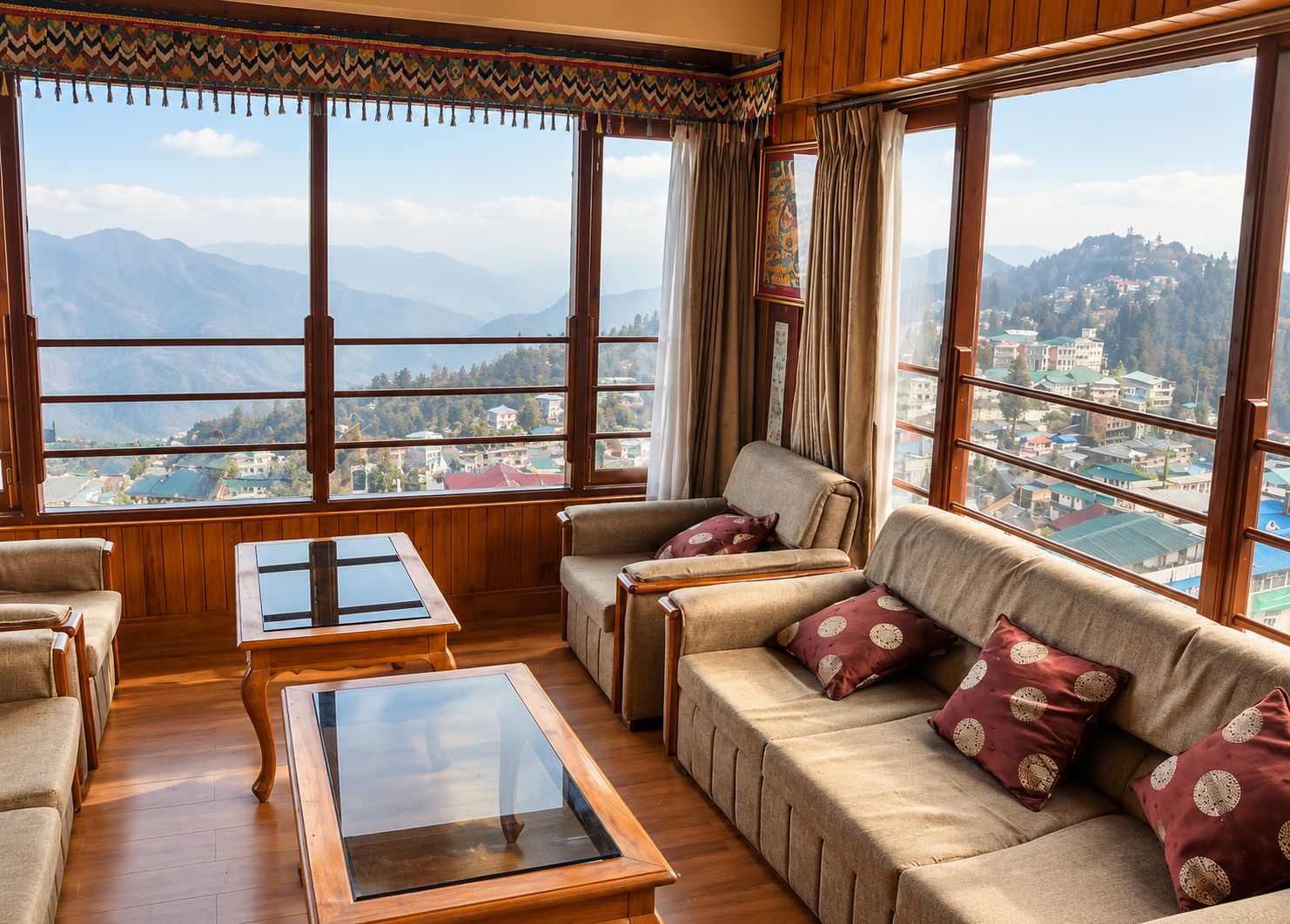 Una habitación con sofá, sillones y una mesa de vidrio, ventanas amplias con vistas a la montaña.