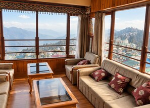 A room with a sofa, armchairs, and a glass-top table, large windows with a mountain view. - Dekeling Hotel (Darjeeling)