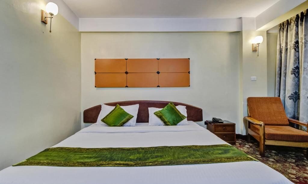 A hotel room with a bed, a nightstand, a chair, and a wall-mounted headboard.