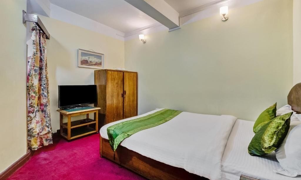 A bedroom with a bed, a television on a stand, a wardrobe, and a curtain.