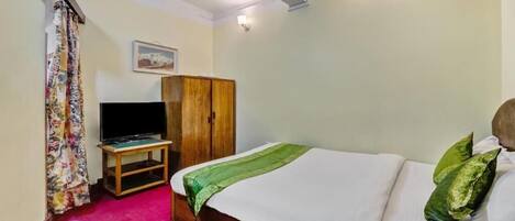 A bedroom with a bed, a television on a stand, a wardrobe, and a curtain.