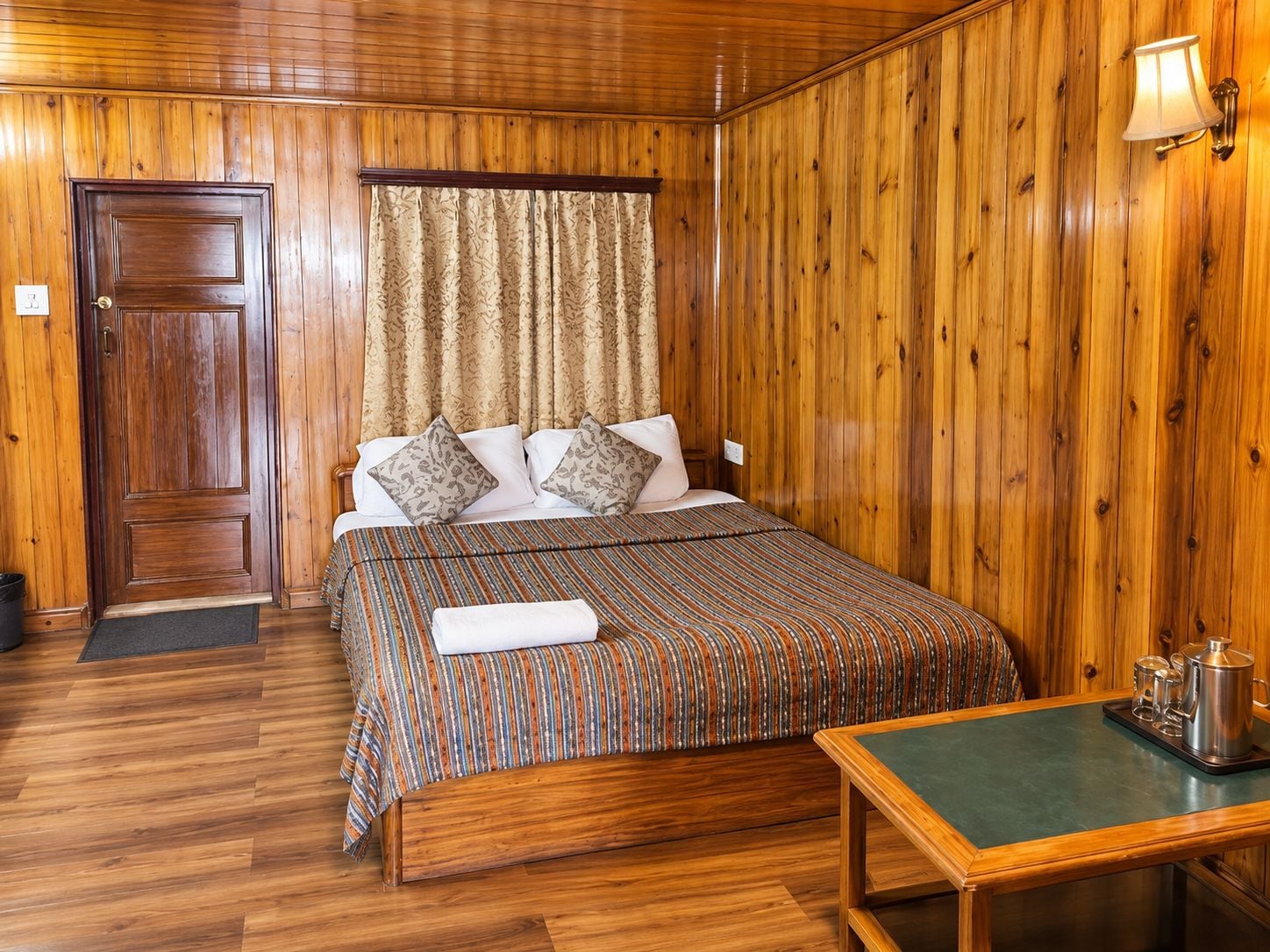 A wooden-paneled room with a bed, a bedside table, and a door.