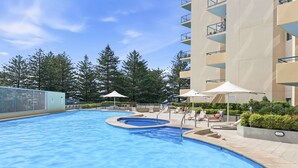 A swimming pool with lounge chairs and umbrellas, surrounded by trees and a multi-story building. - MetaWise BNB Modern Studio in Central Cronulla 2 (Cronulla)