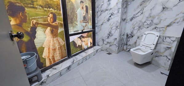 A bathroom with a toilet, marble walls, and a window with a view of a park. - Hotel HR Gold (Ahmedabad)