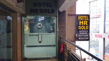 A hotel entrance with a reception desk, a sign for 'Hotel HR Gold' and 'JACUZZ ROOMS 2nd FLOOR,' and a visible fire extinguisher.