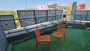 A rooftop terrace with artificial grass, two orange chairs, and a metal railing. - Hotel HR Gold (Ahmedabad)