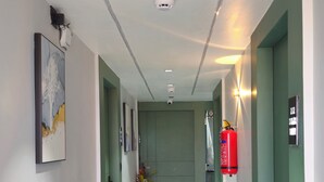 A hallway with a green door, a fire extinguisher, and a security camera. - Hotel HR Gold (Ahmedabad)