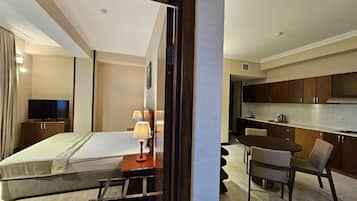A hotel room with a bed, bedside table, lamp, and a view of the kitchen area.