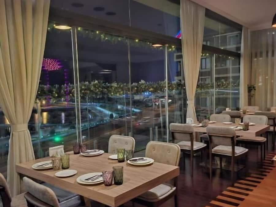 Un restaurante con mesas dispuestas para comer, amplias ventanas con cortinas y vistas a la ciudad.