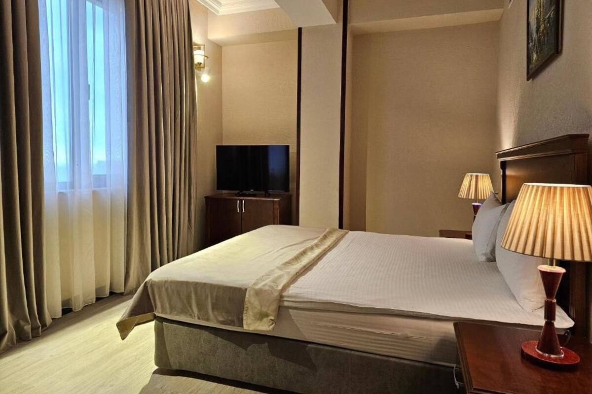 A hotel room with a bed, a television, a lamp, and a window with curtains.