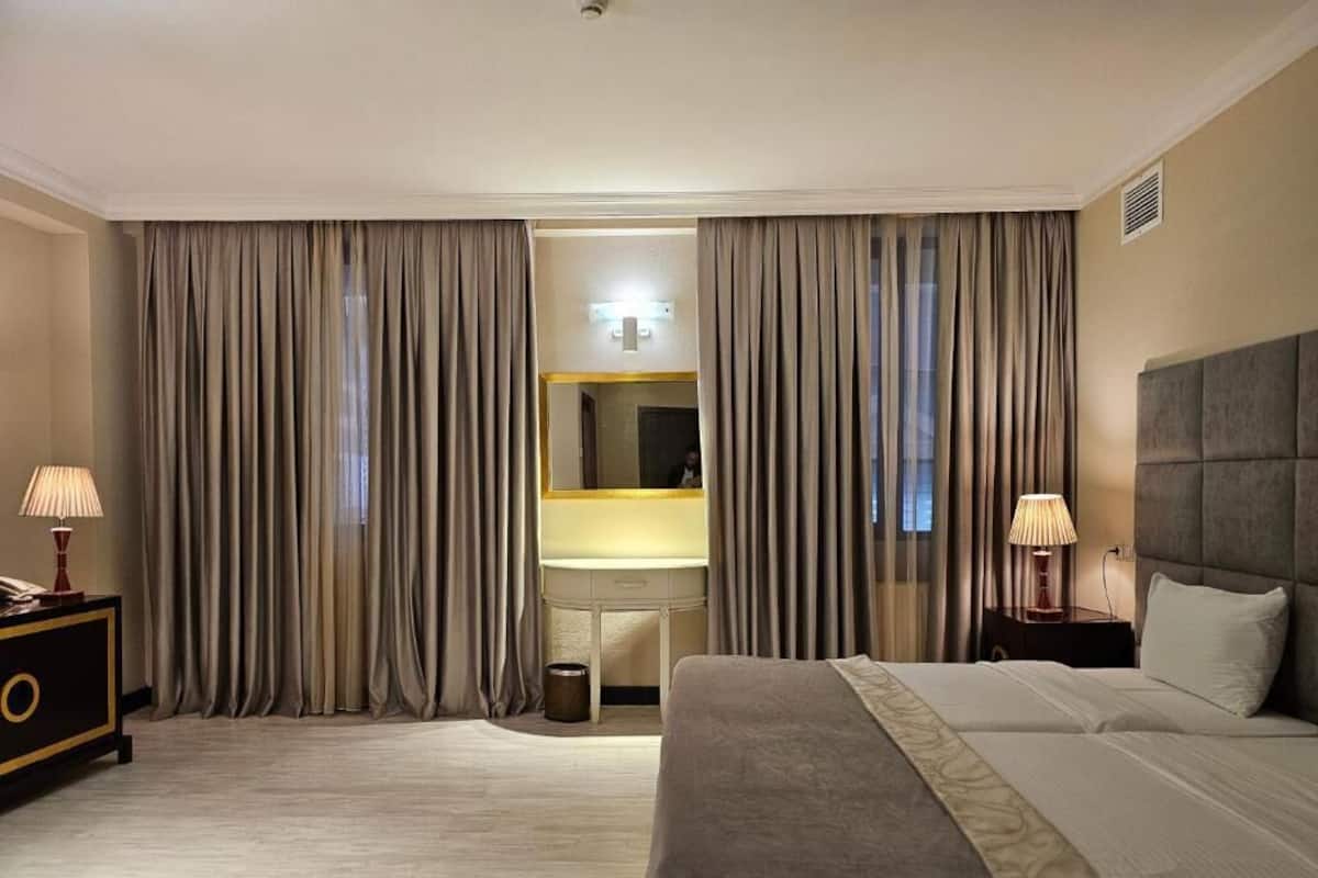 A hotel room with a large bed, two bedside tables, a desk with a chair, and curtains.