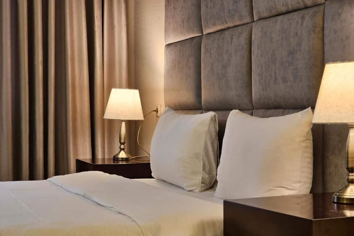 A hotel room with a bed, two bedside lamps, and a headboard.