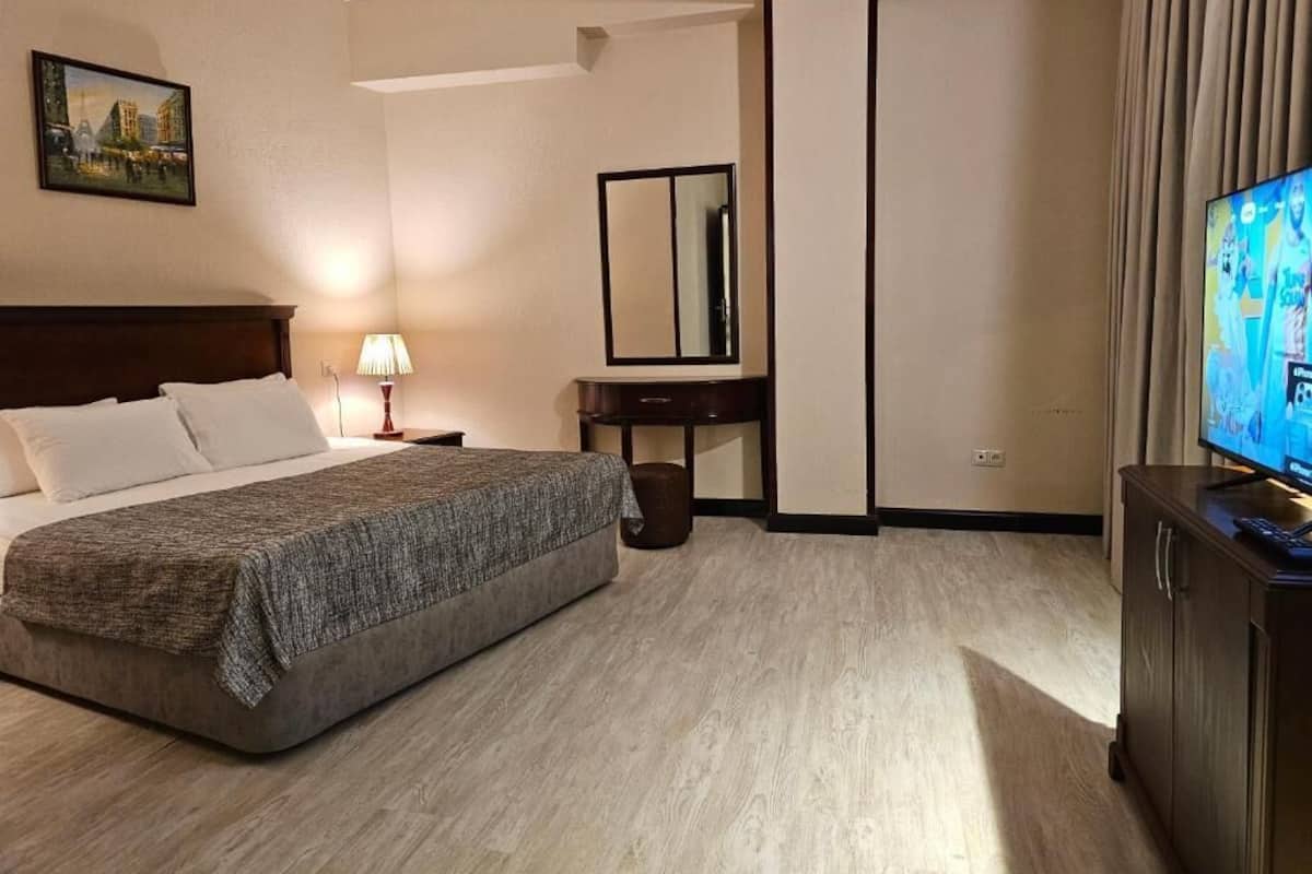 A hotel room with a bed, a desk, a mirror, a television, and a painting on the wall.