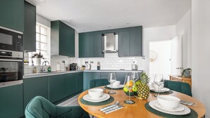 A modern kitchen with teal cabinetry, a wooden dining table set with white plates, and a pineapple centerpiece. - Luxury 2 Bedroom Apartment near London Bridge • Sleeps 6 • Tube Across Street (London)