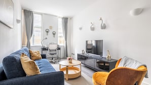 A modern living room with a sofa, armchair, TV, and a desk with a computer. - Luxury 2 Bedroom Apartment near London Bridge • Sleeps 6 • Tube Across Street (London)