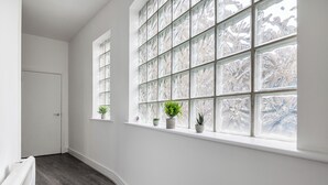 A hallway with a white door, a window with frosted glass, and potted plants on the windowsill. - Luxury 2 Bedroom Apartment near London Bridge • Sleeps 6 • Tube Across Street (London)