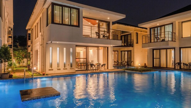 A modern two-story building with a swimming pool, large windows, and outdoor seating areas. - Staymaster Aqua Cottage 3BR Villa  (Vagator)