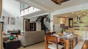 A spacious living area with a sofa, dining table, and chairs, a staircase, and a kitchen area. - Staymaster Aqua Cottage 3BR Villa  (Vagator)