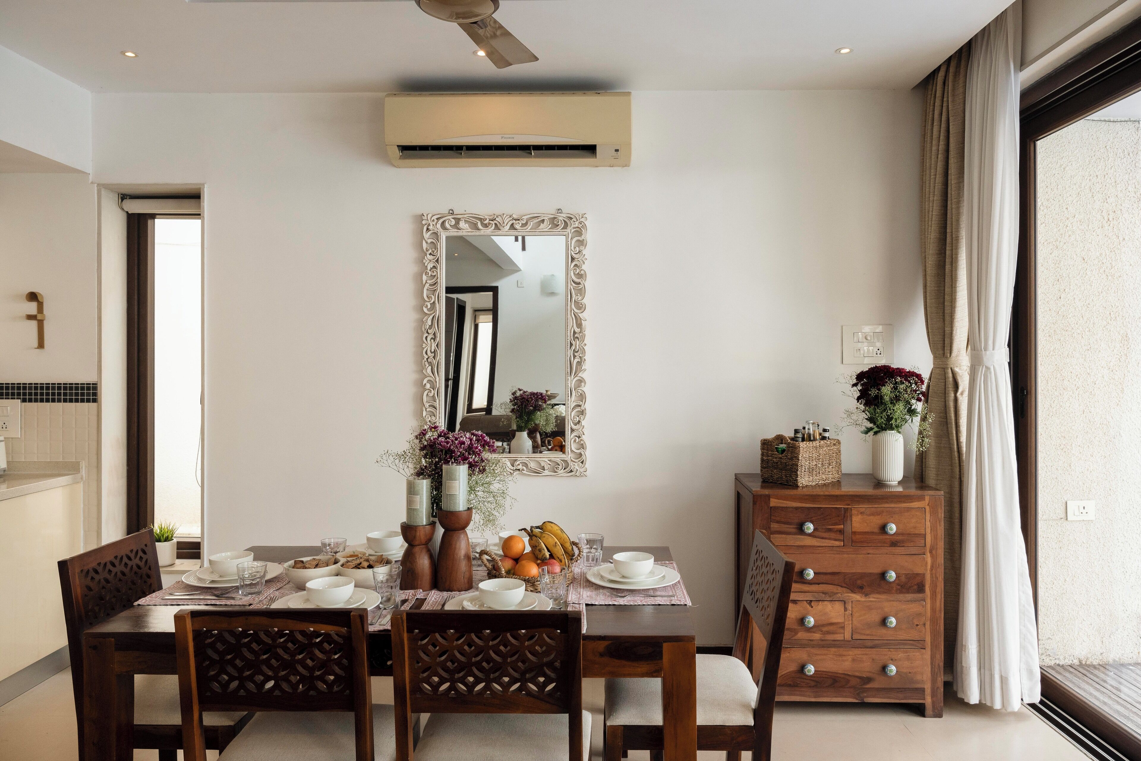 A dining area with a table set for four, a mirror on the wall, and a wooden cabinet with drawers.