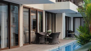 A modern outdoor pool area with a wooden deck, a table with chairs, and a potted plant. - Staymaster Aqua Cottage 3BR Villa  (Vagator)