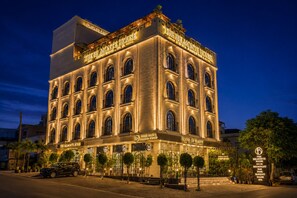 Un hôtel à plusieurs étages, doté d’une enseigne lumineuse, d’une entrée imposante et d’un parvis aménagé avec des arbres.