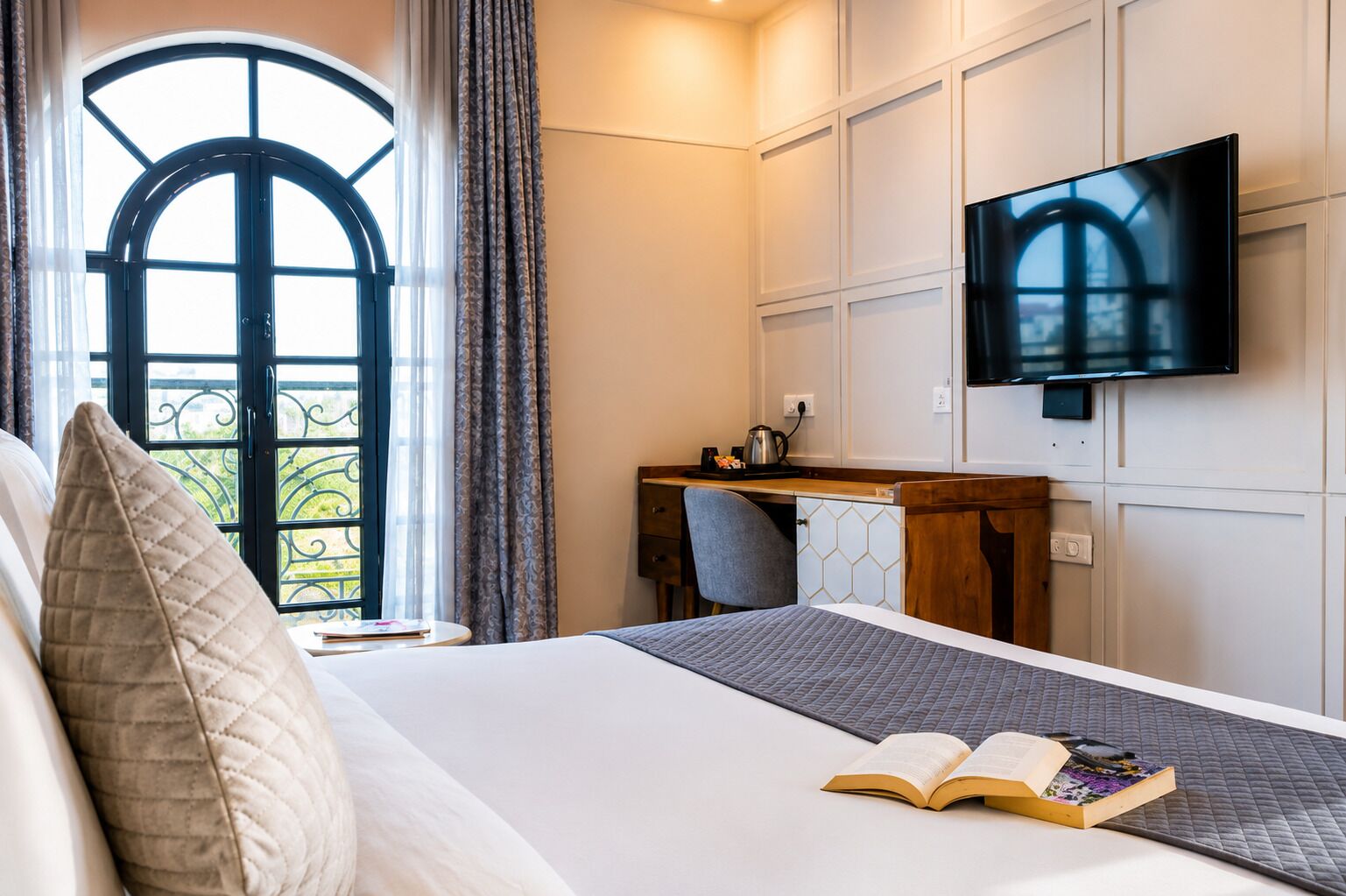 Una habitación de hotel con cama, escritorio, televisor y ventana con cortinas.