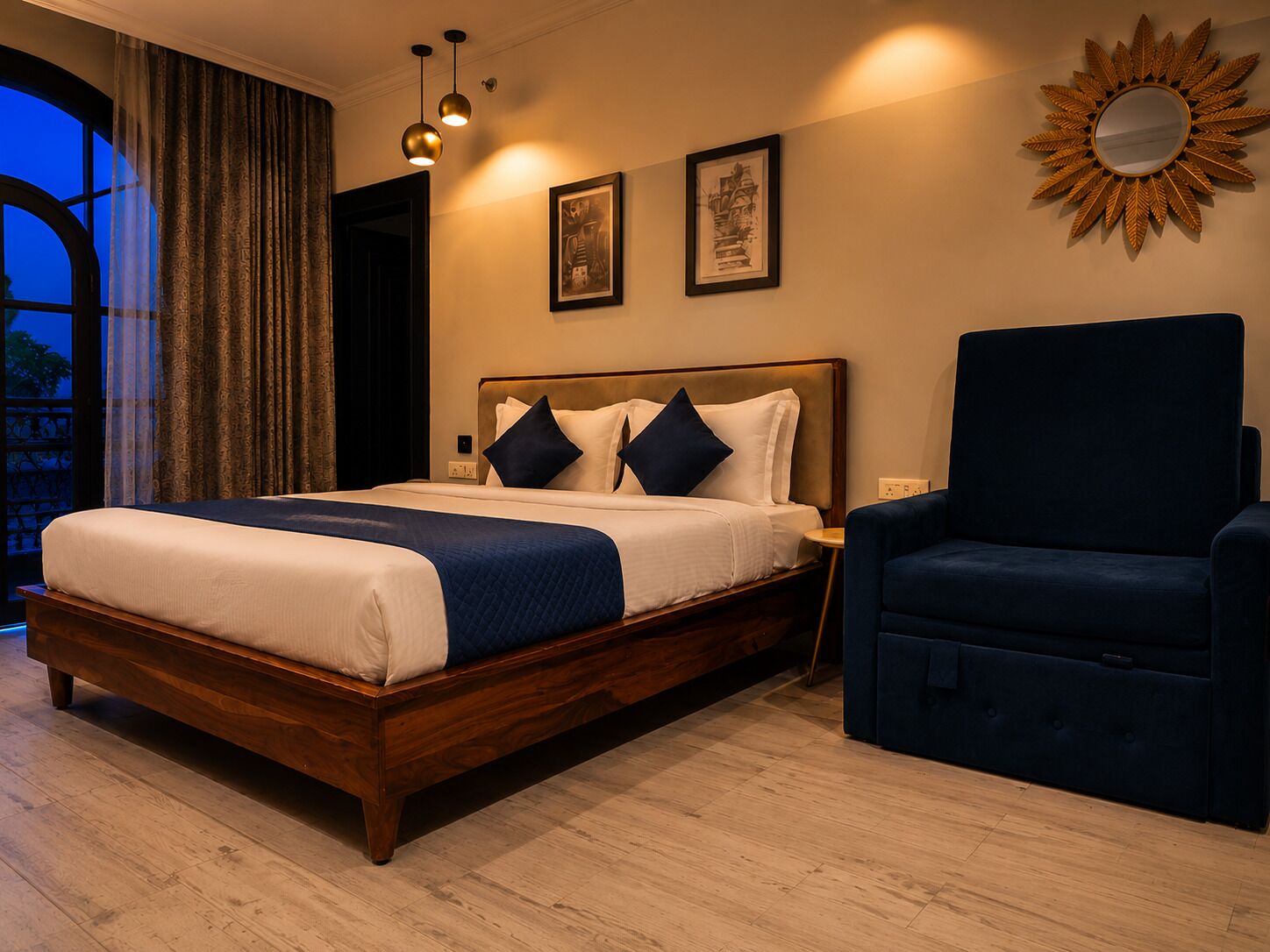 A hotel room with a wooden bed, a dark armchair, a large mirror, and two framed pictures on the wall.