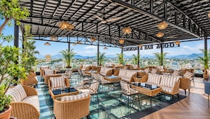 An outdoor seating area with wicker furniture and glass tables, overlooking a cityscape. - Belmonte House, Udaipur (Udaipur)