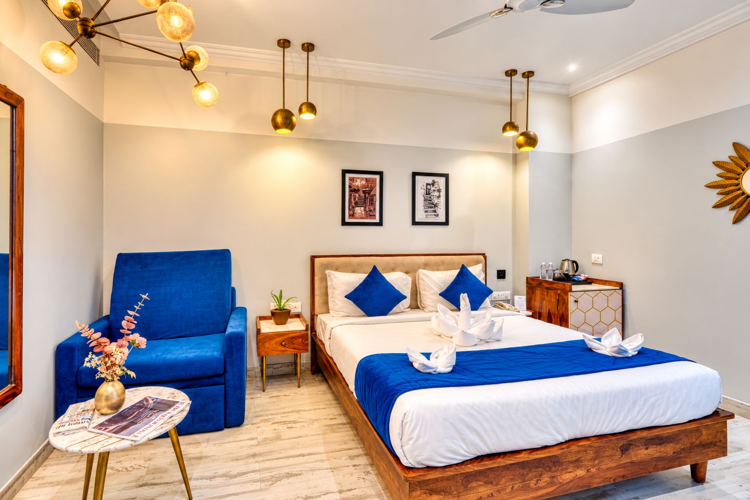 A hotel room with a large bed, a blue armchair, a small table with a magazine, and a nightstand with a plant.