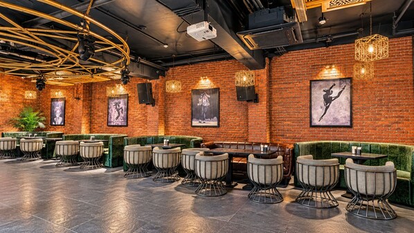 A restaurant interior with brick walls, green cushioned seating, and framed artwork. - Belmonte House, Udaipur (Udaipur)