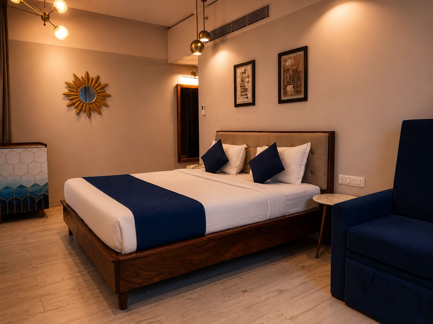 A hotel room with a wooden bed, a blue chair, a mirror, and artwork on the wall.