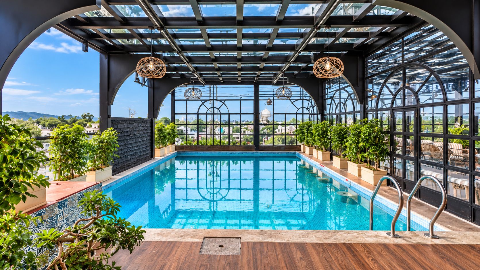 An indoor swimming pool with a glass ceiling, surrounded by potted plants and a wooden deck.