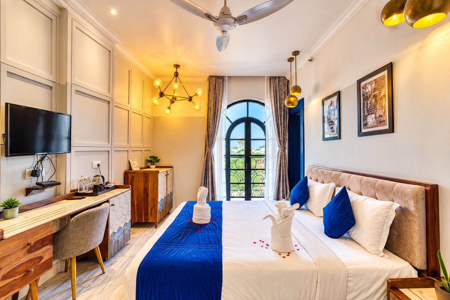Quarto de hotel com cama, escrivaninha, cadeira, televisão e vista para o verde pela janela.
