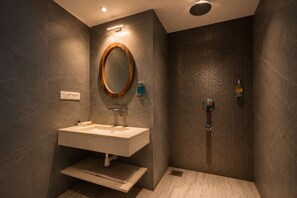 Une salle de bain moderne avec un meuble-lavabo, un grand miroir, une douche avec un mur carrelé et un luminaire.