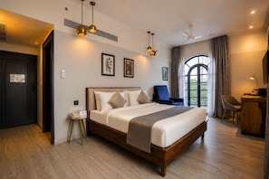 Une chambre d’hôtel avec un grand lit, un bureau, une chaise, une petite table et une fenêtre donnant sur un beau paysage.